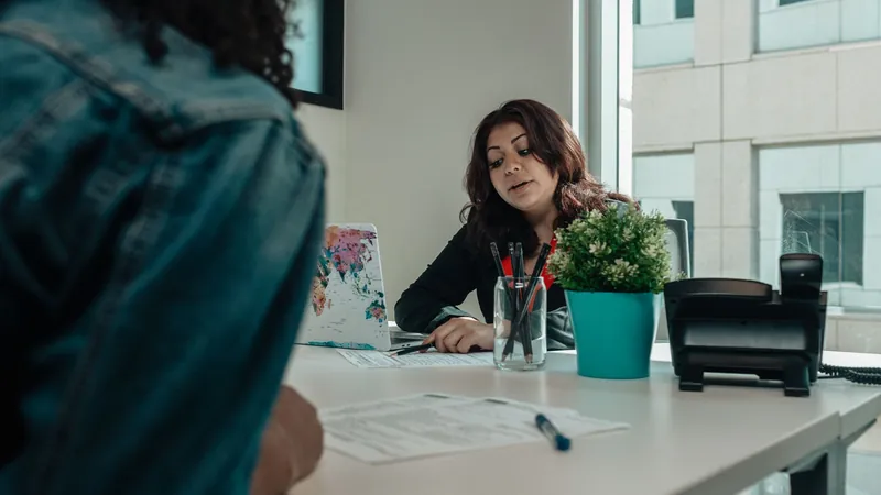 Agent at an office desk going over paperwork with a client, a desk phone beside her