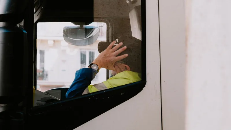 Truck driver in a high-visibility jacket resting a hand on his cap inside the cab