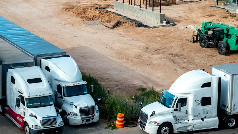 Three white semi trucks parked together beside a construction site