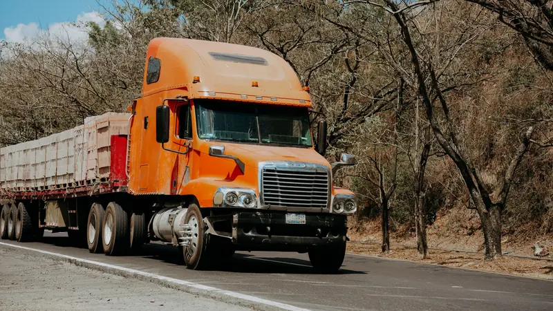 Orange semi truck hauling a trailer along a two-lane highway
