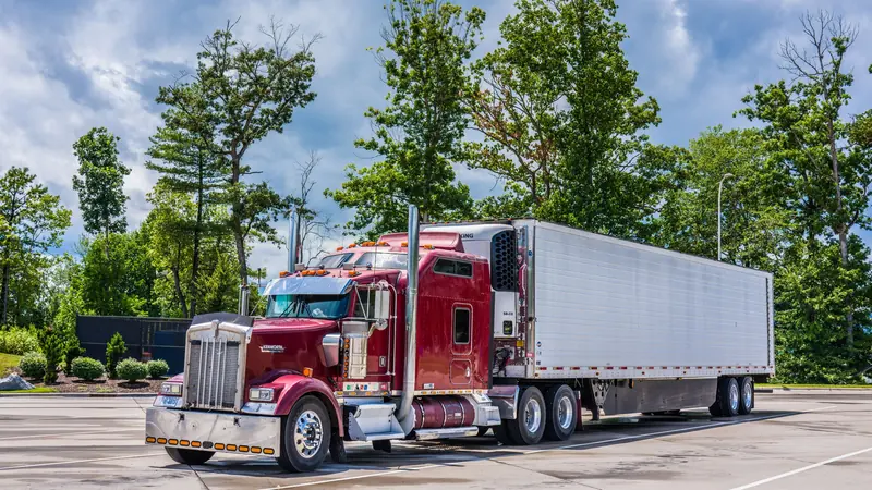 Red semi truck with a refrigerated trailer parked in a truck lot