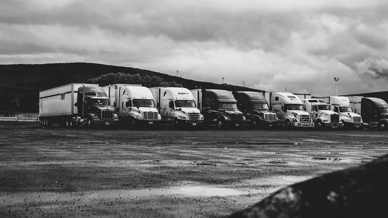 Row of parked semi trucks under a cloudy sky, in black and white