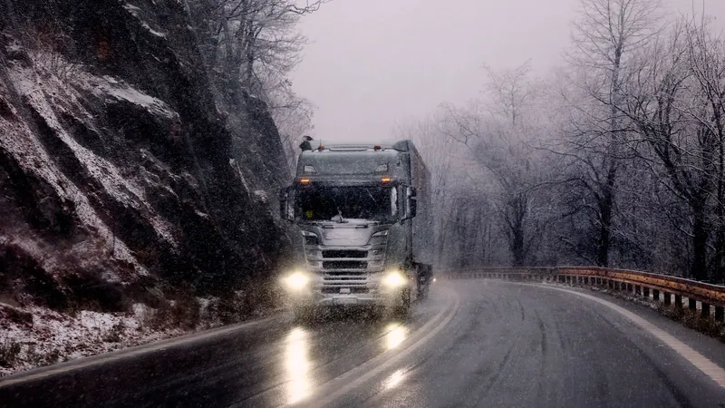 Truck with its headlights on driving down a snowy mountain road